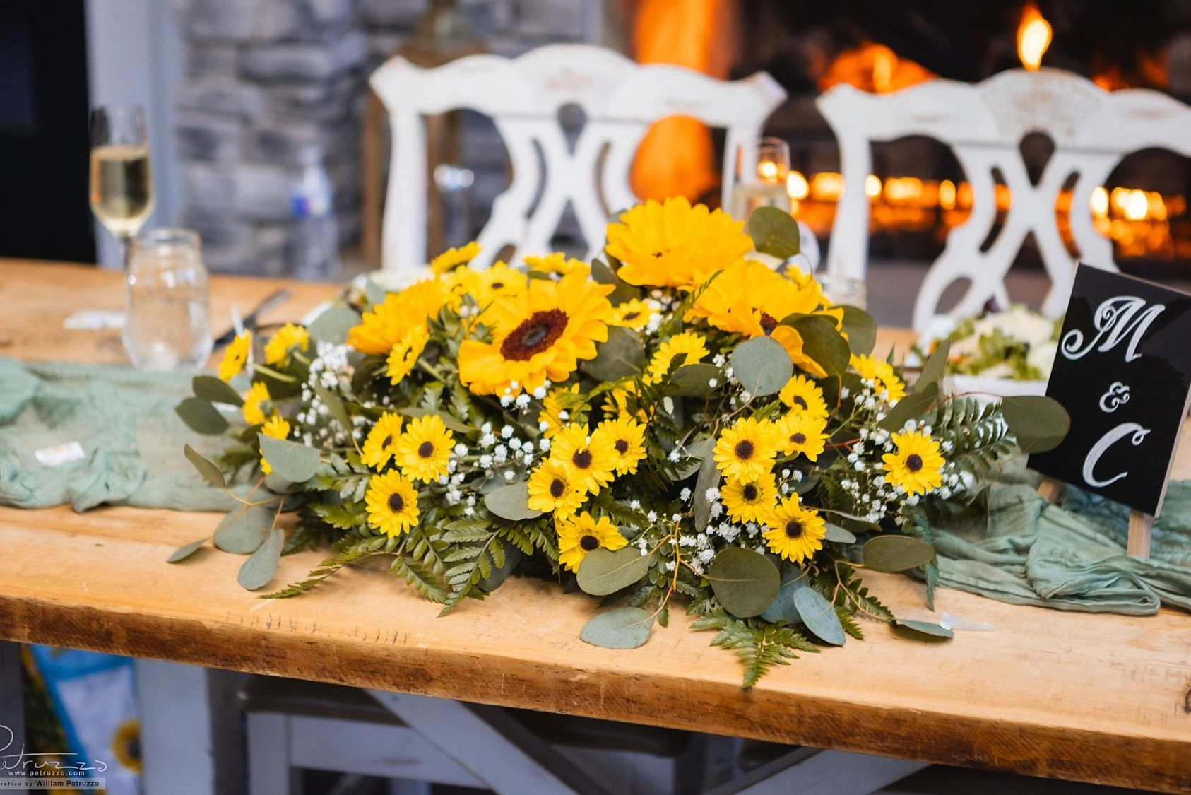 A long sunflower and daisy arrangement on a rustic table by the fire