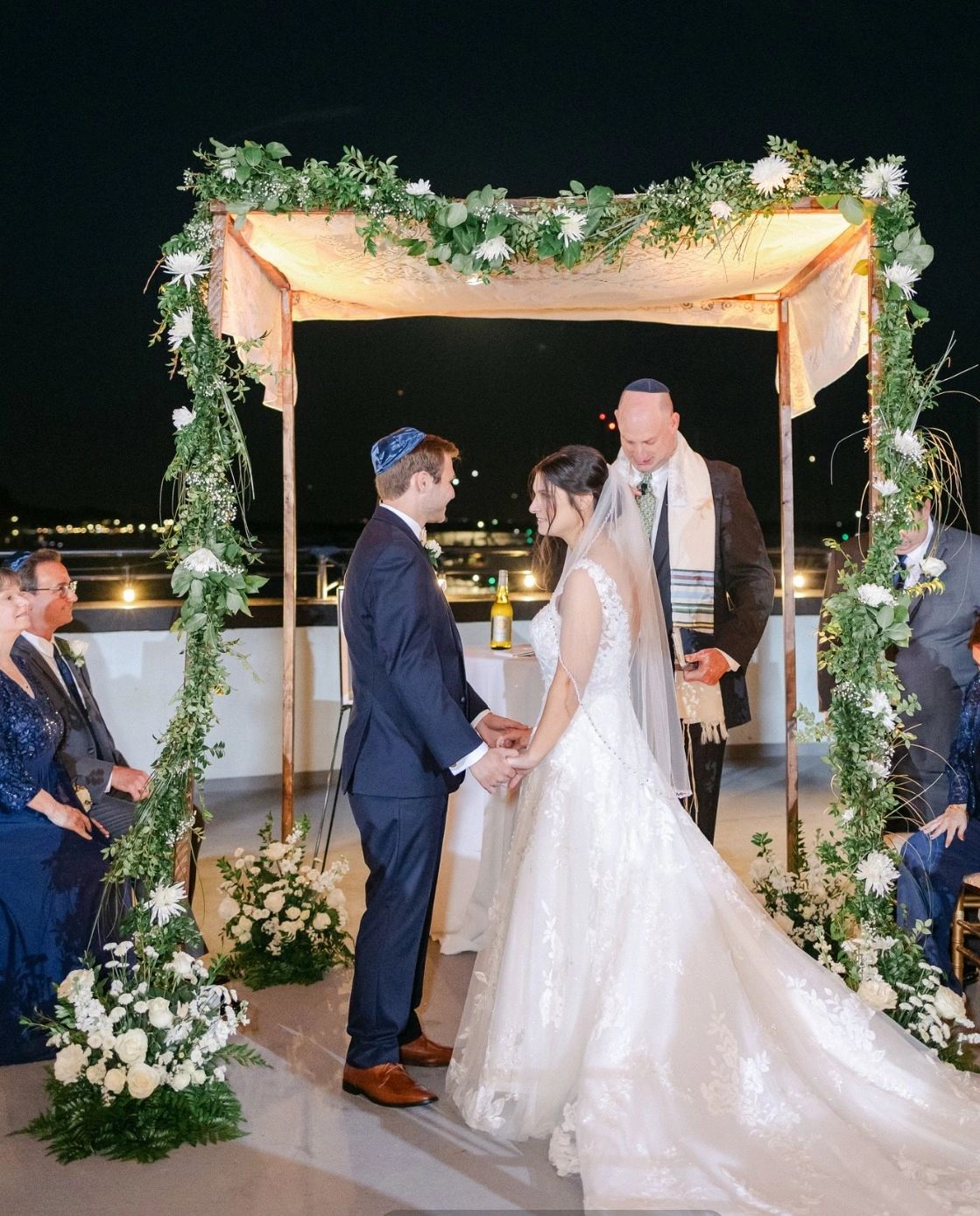 A ceremony beneath a lit floral arch after dark on the waterfront