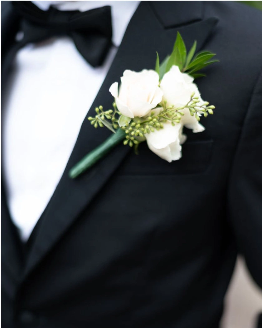 A white rose buttonhole with seeded eucalyptus pinned to a black lapel