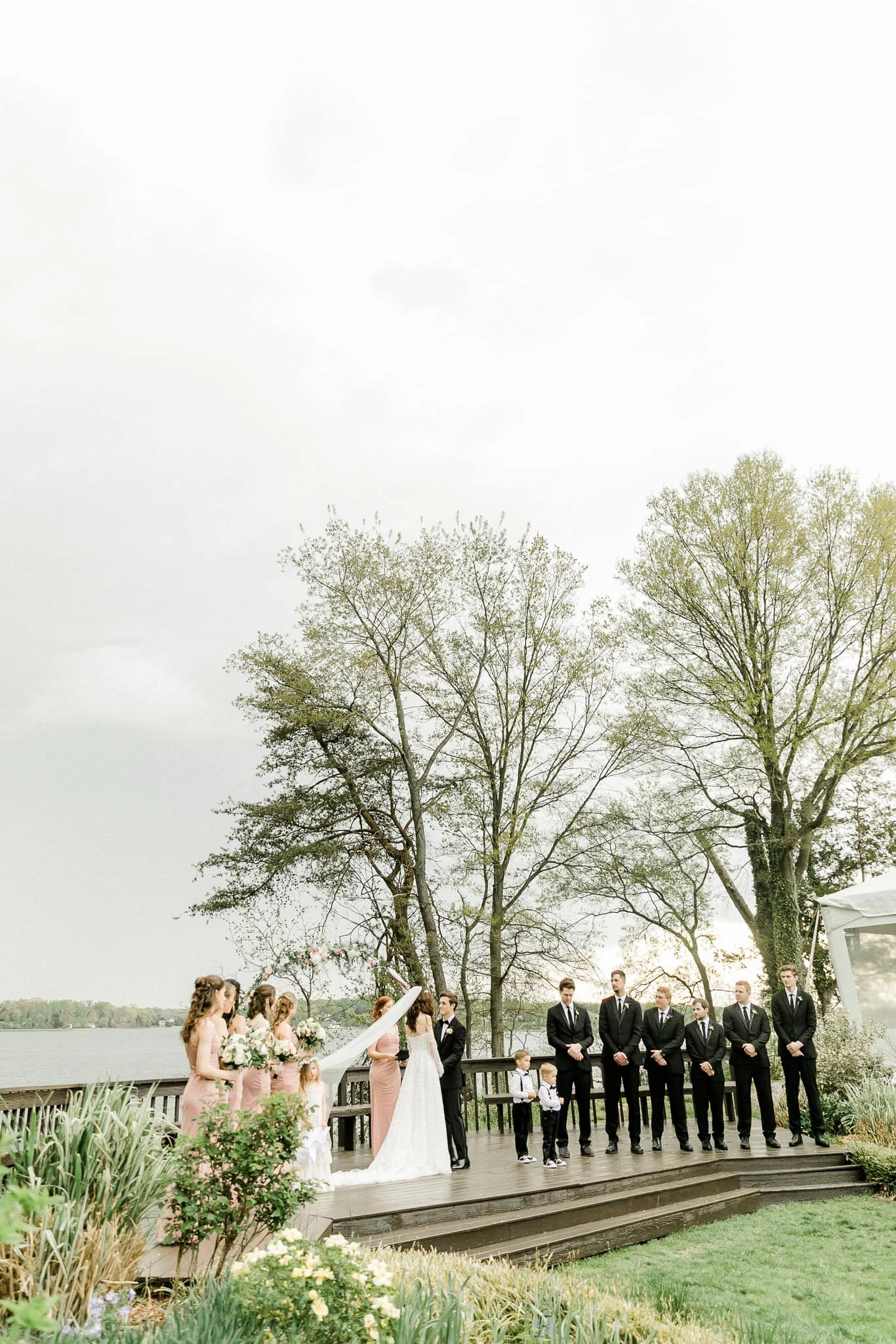 The bridal party gathered by the water beneath spring trees