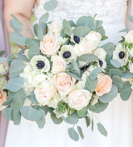 Bridal bouquet of blush garden roses, white anemones and eucalyptus held by a bride in lace