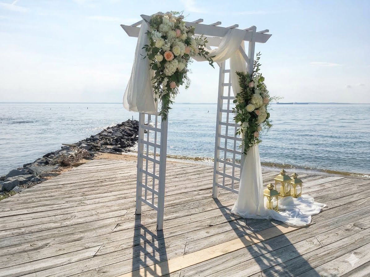 Waterfront ceremony arch dressed in white roses and hydrangea on a pier over the Chesapeake Bay, by Little House of Flowers
