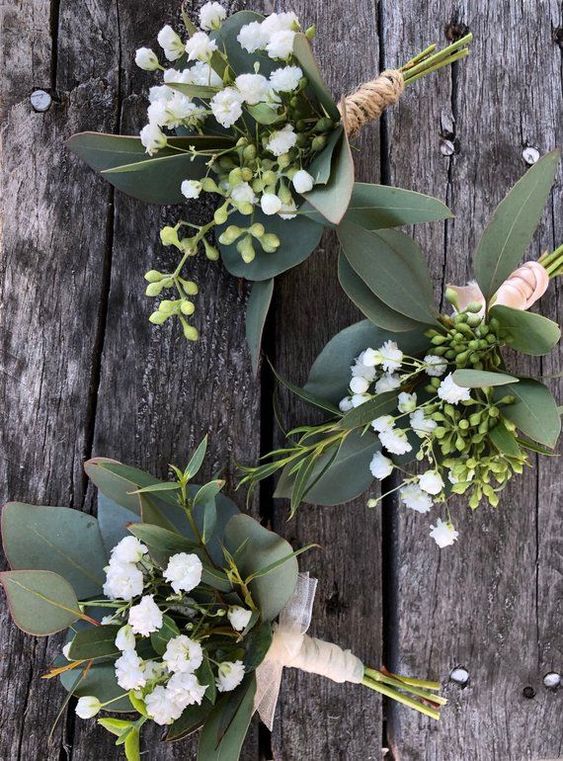 Three buttonholes of eucalyptus, seeded gum and gypsophila, tied with twine, laid on weathered wood