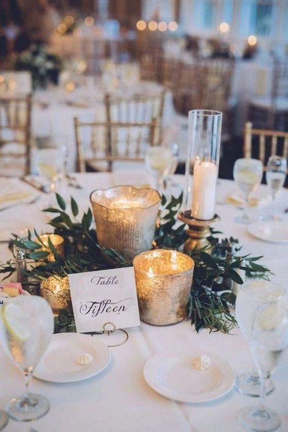 Gold mercury votives and a greenery wreath around a candle at a formal table
