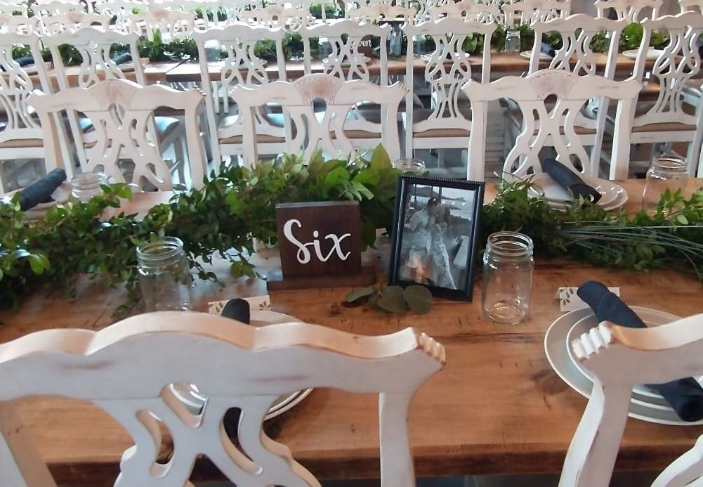 A farm table laid with a greenery runner, mason jars and a wooden table number