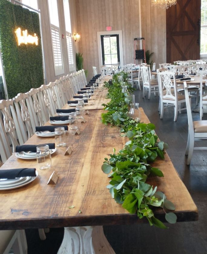 A long farm table run end to end with a lush greenery garland and navy napkins